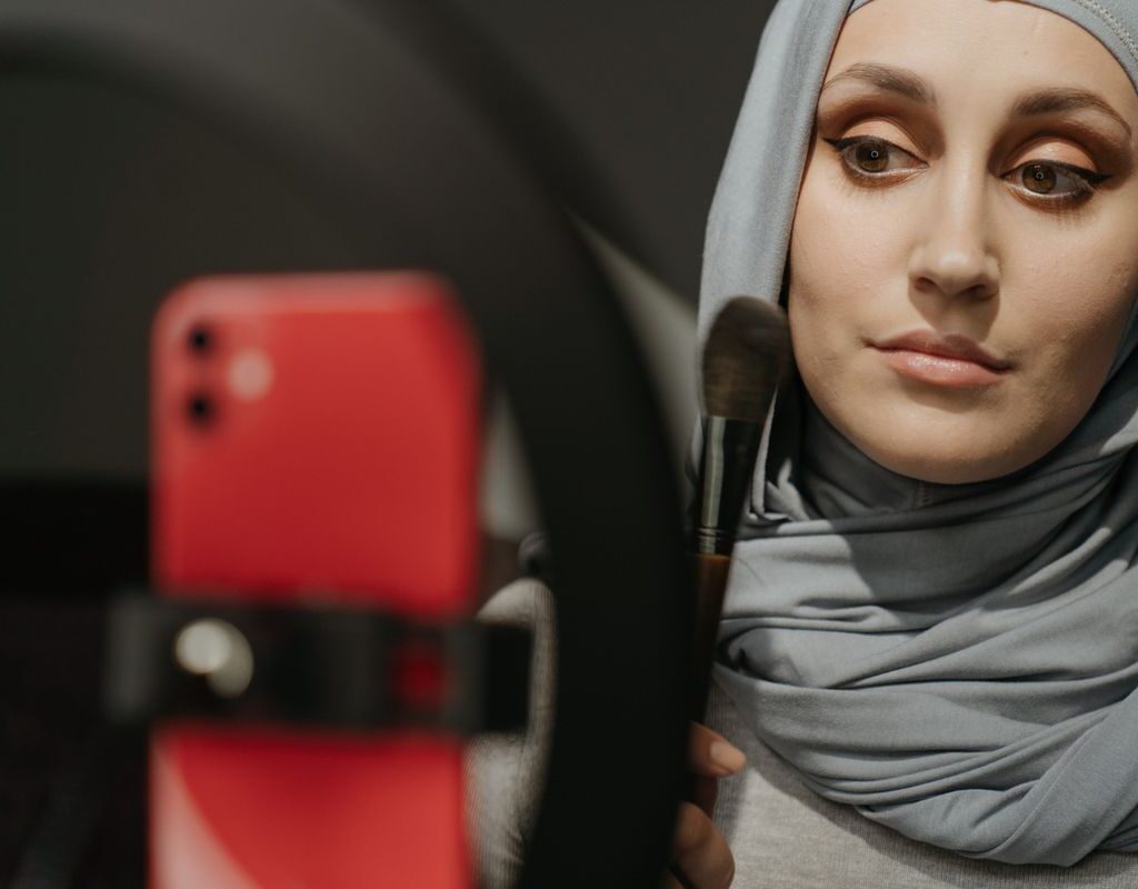 Frau schminkt sich und nutzt dabei ein Smartphone