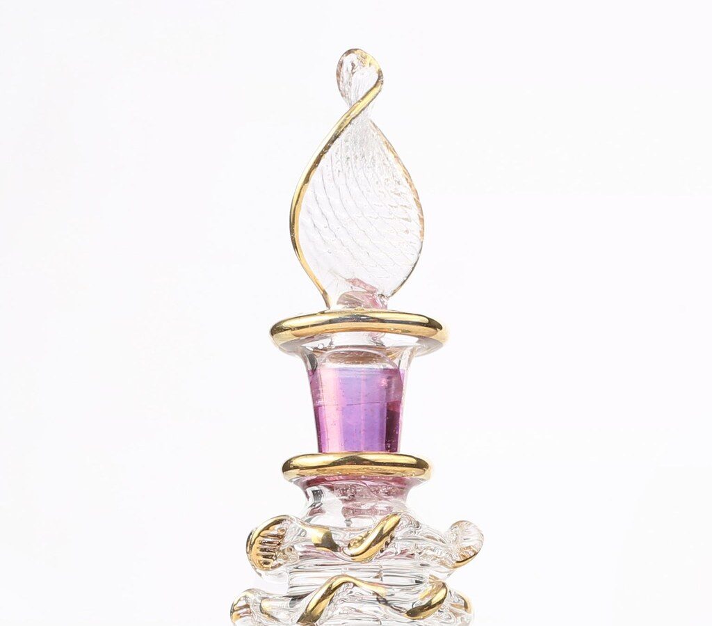 Verzierter Parfümflakon aus Glas mit Goldrändern und violettem Hals vor hellem Hintergrund