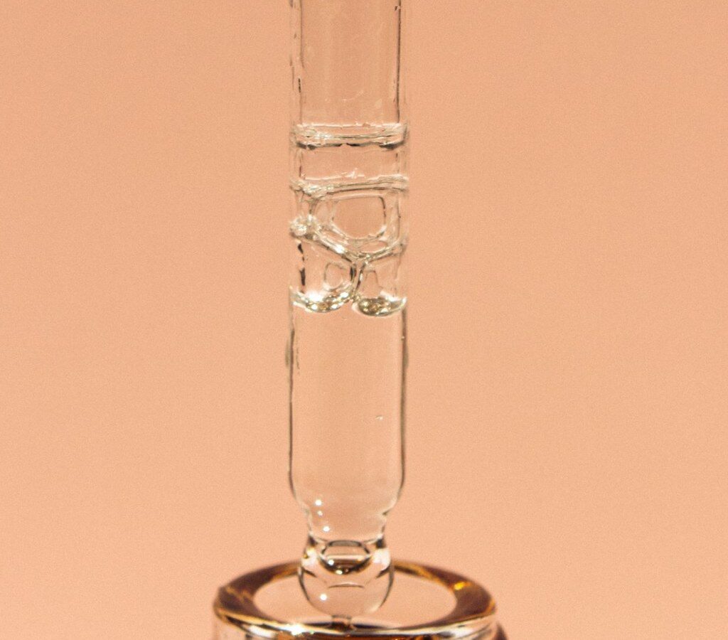 Glaspipette über einer Flasche mit Pflegeserum vor pfirsichfarbenem Hintergrund