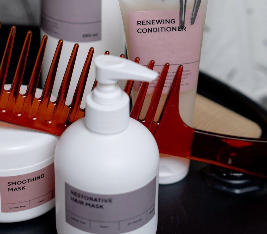 Weiße Pflegeflaschen, Tiegel und Tube für die Haarpflege mit orangefarbenem Kamm auf einem schwarzen Tablett