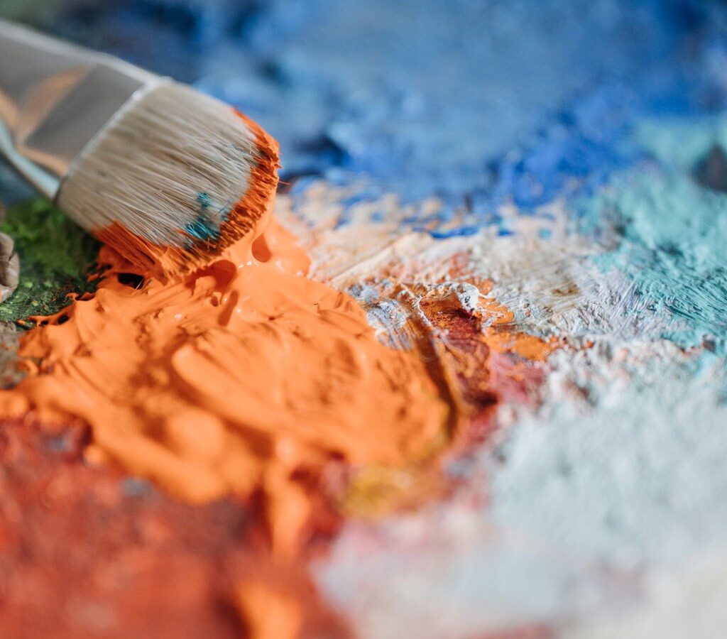 Pinsel mit orangefarbener Farbe auf einer Palette mit blauen und türkisen Farbflächen