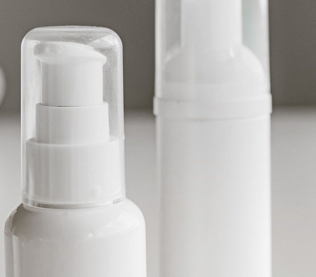 Zwei weiße Pumpflaschen für Kosmetikprodukte auf heller Fläche
