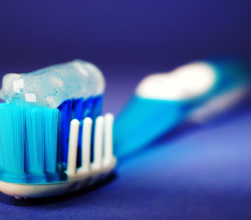 Zahnbürste mit blau-weißem Zahnpastagel vor blauem Hintergrund