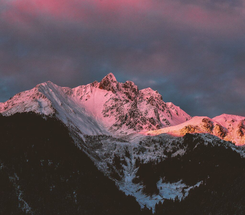 Schneebedeckte Berge im rosafarbenen Licht der aufgehenden Sonne unter bewölktem Himmel