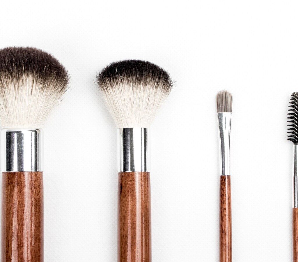 Vier Make-up-Pinsel mit Holzgriff und Metallzwinge nebeneinander auf weißem Hintergrund
